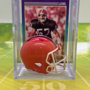 May include: A miniature orange and white football helmet in a clear plastic display case with a Score football card featuring a player wearing a brown and white uniform. The card has the text "BROWNS" on the bottom.