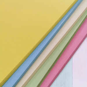 May include: A stack of colorful foam sheets in shades of yellow, blue, cream, green, and pink. The sheets are arranged diagonally, showcasing their edges and colors. The image is well-lit, highlighting the smooth texture of the foam.