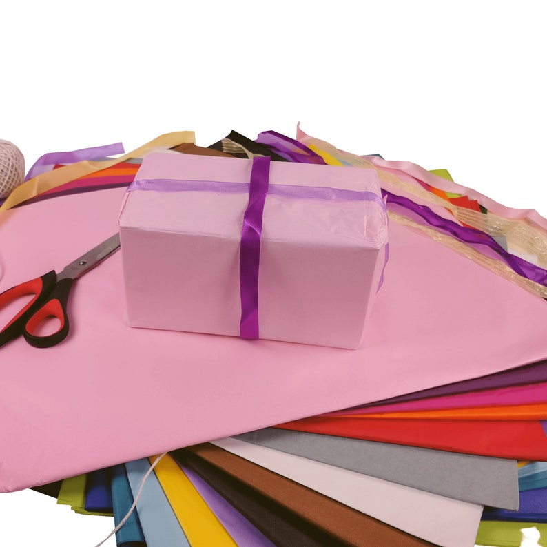 May include: A pink gift box with a purple ribbon, surrounded by a variety of colorful tissue paper and a pair of scissors.