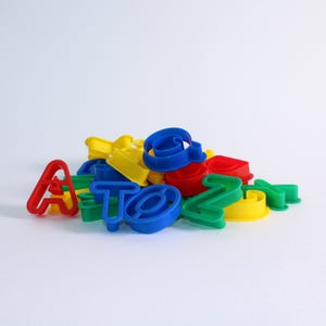 Puede incluir: Un montón de cortadores de galletas de plástico de colores en forma de alfabeto en rojo, amarillo, azul y verde.