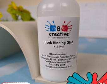 May include: A clear plastic bottle of B Creative Book Binding Glue containing 100ml of adhesive. The white label features blue and red handprint graphics, the text B creative, and contact details. A small graphic notes it dries clear.