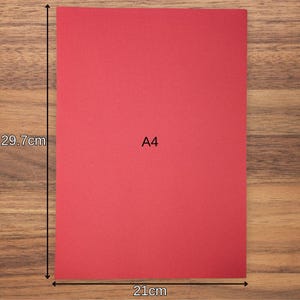 May include: A rectangular sheet of red paper labelled A4 in the centre. The paper is measured with arrows indicating a height of 29.7 cm and a width of 21 cm. The surface of the paper appears flat and solid red, providing a clear visual reference for size.