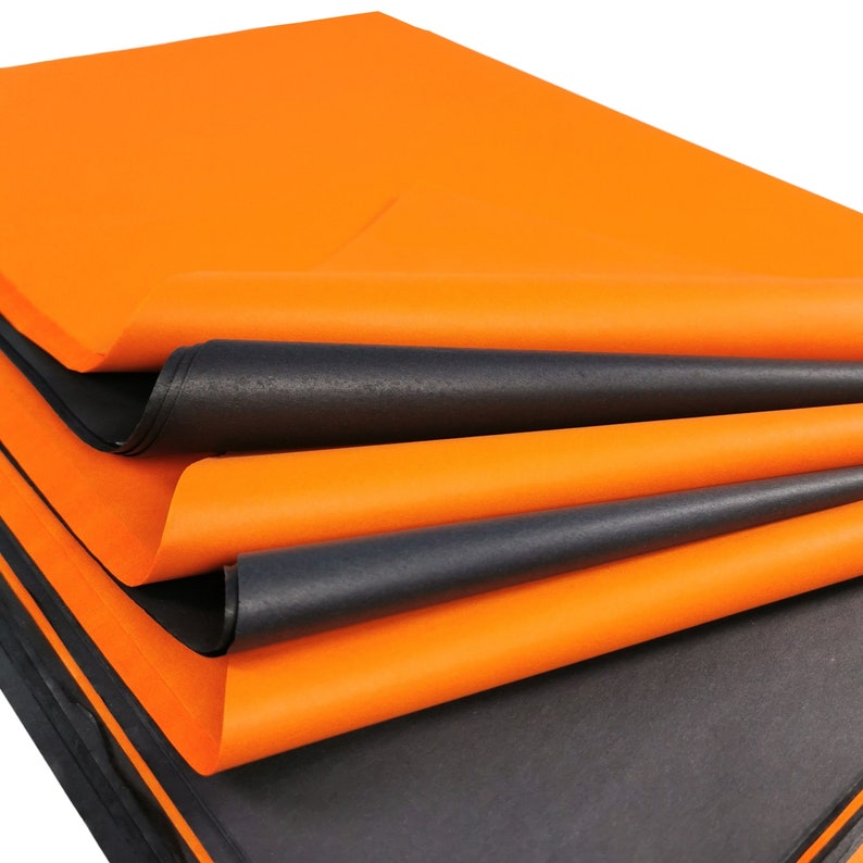 May include: A stack of orange and black tissue paper. The paper is folded and layered, showing the different colors.
