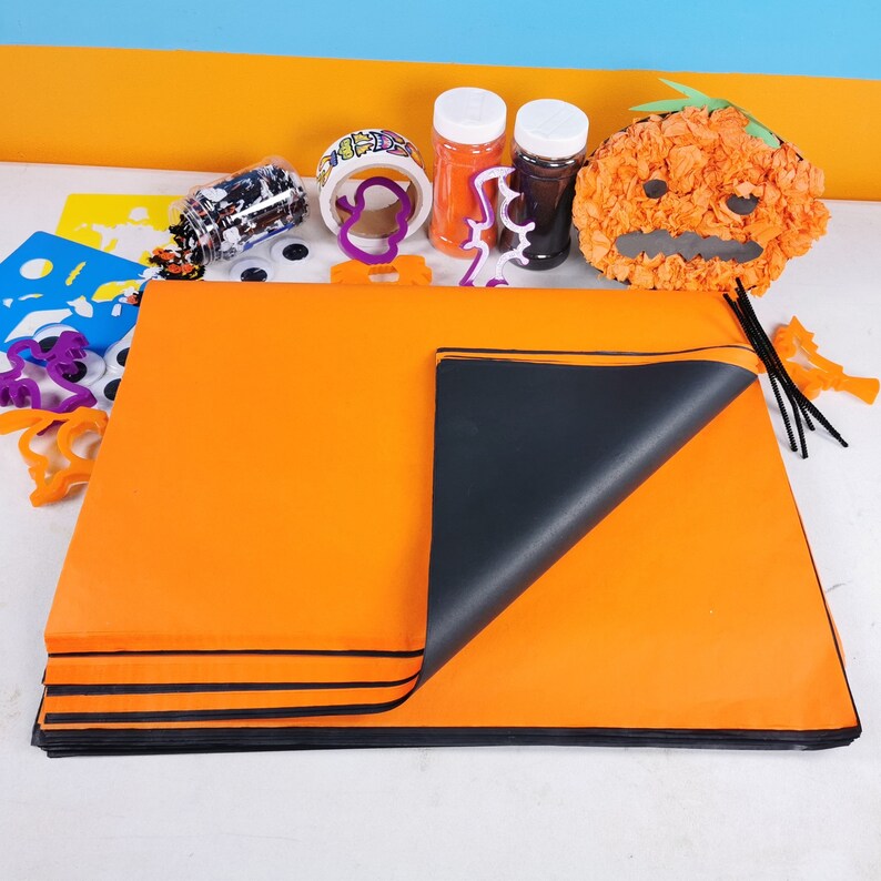 May include: A set of craft supplies for making Halloween decorations. The set includes orange and black craft paper, googly eyes, a pumpkin-shaped tissue paper craft, and two containers of glitter.