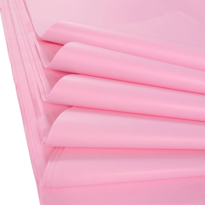 May include: Stack of pink tissue paper, folded and layered, showing the soft texture and delicate color.