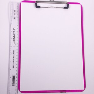 Puede incluir: Un portapapeles rosa con una hoja de papel blanca en su interior. El portapapeles tiene un clip de metal y una regla en el lado izquierdo con el texto "KF01108", "Q-CONNECT" y "SHATTER RESISTANT".