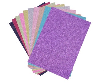 Könnte beinhalten: Ein Stapel aus 12 Blättern Glitzerpapier in verschiedenen Farben, darunter Lila, Rosa, Blau, Grün und Gold. Die Blätter sind fächerförmig angeordnet.