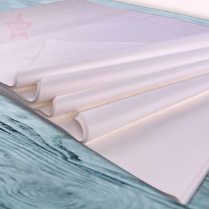 May include: A stack of white tissue paper, folded and displayed on a blue wooden surface. The tissue paper is smooth and has a subtle sheen.