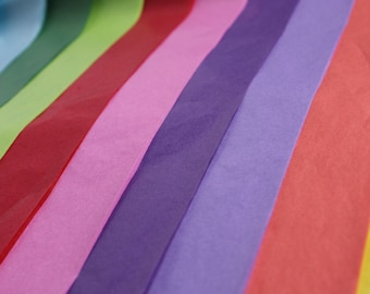 Könnte beinhalten: Eine Sammlung von bunten Seidenpapierbögen in verschiedenen Blautönen, Grüntönen, Rottönen, Rosatönen, Violetttönen und Orangetönen. Das Seidenpapier ist fächerförmig angeordnet, wobei die Farben ineinander übergehen.