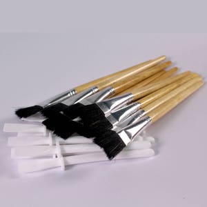 May include: A set of ten paint brushes with wooden handles and black bristles. The brushes are bundled together with white plastic handles.