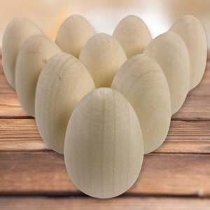 May include: A group of ten smooth, unfinished wooden eggs arranged in a triangular shape on a wooden surface.