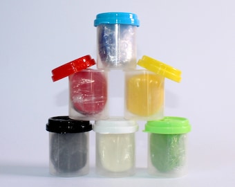 Könnte beinhalten: Sechs kleine Plastikbehälter mit Deckeln, die in Pyramidenform gestapelt sind. Die Behälter sind mit verschiedenfarbiger Modelliermasse gefüllt, darunter blau, rot, gelb, weiß, schwarz und grün.