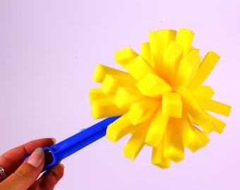 Könnte beinhalten: Ein gelber Schwamm-Reinigungswerkzeug mit einem blauen Kunststoffgriff. Der Schwamm ist blumenförmig mit vielen langen, dünnen Strähnen.
