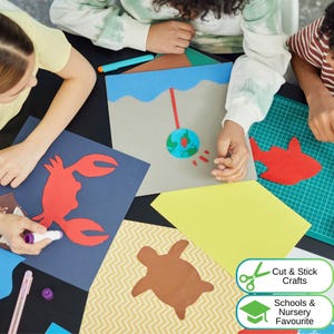 May include: A collection of paper craft projects featuring a red crab cutout on dark blue paper, a brown turtle on chevron paper, a red fish on a green cutting mat, and a globe illustration on grey paper with the text Cut & Stick Crafts.