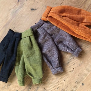 Puede incluir: Cuatro pares de pantalones de diferentes colores y patrones. Los pantalones están hechos de una tela suave y texturizada. Los colores son negro, verde, marrón y naranja.