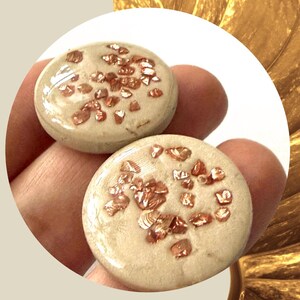 May include: Two round, beige-colored decorative stones with copper-colored flecks. The stones are smooth and shiny, with a slightly raised surface. The stones are likely used for home decor or craft projects.