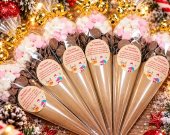 May include: Five cone-shaped clear plastic bags filled with hot chocolate mix, chocolate chips, and pink and white marshmallows. Each bag is tied with a gold ribbon and features a round sticker labeled Reindeer Hot Chocolate.