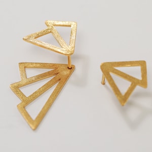 Op de afbeelding: Een paar gouden geometrische oorbellen. Eén oorbel heeft een enkele driehoeksvorm, terwijl de andere drie overlappende driehoeken heeft.