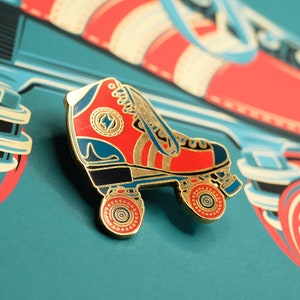 Puede incluir: Un pin de patín de ruedas de color dorado con detalles de esmalte rojo y azul. El pin presenta un diseño detallado con ruedas y una forma de patín clásica.