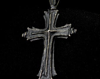 May include: A silver-toned cross pendant with a detailed, ornate design. The cross has a pointed top and a slightly rounded bottom.
