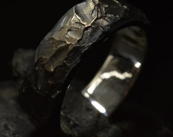 May include: A silver ring with a textured, hammered finish. The ring has a wide band and a slightly rounded edge.