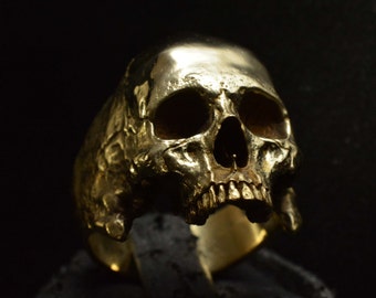 Puede incluir: Un anillo de calavera de tono dorado con detalles intrincados. La calavera se representa con un diseño realista y detallado, que incluye cuencas de los ojos, una nariz y una boca.
