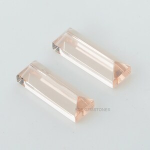 May include: Two pale pink, rectangular, faceted gemstones. The gemstones are cut into a long, narrow shape with a pointed end.