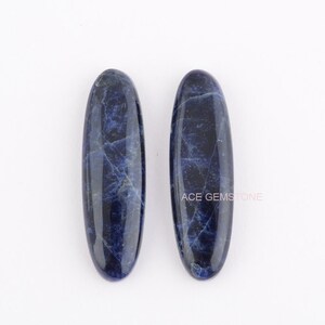 May include: Two oval-shaped, dark blue, polished, natural sodalite stones. The stones have a marbled pattern.