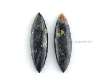 May include: Two black and gray gemstone cabochons with a marbled pattern and gold flecks. The cabochons are shaped like a long oval.