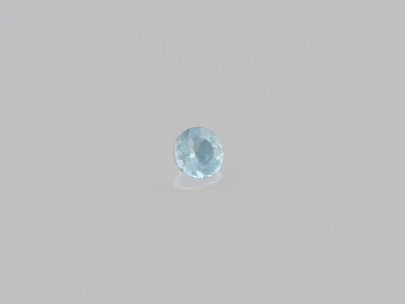 May include: A light blue round gemstone with facets.