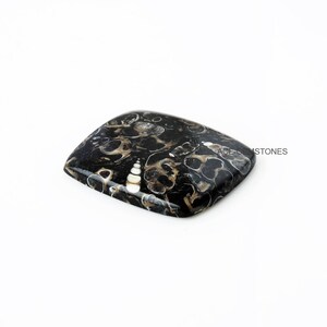 May include: A black, white, and brown agate cabochon with a square shape. The stone has a swirling pattern of black, white, and brown.