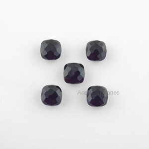May include: Five black cushion-cut gemstones on a white background.