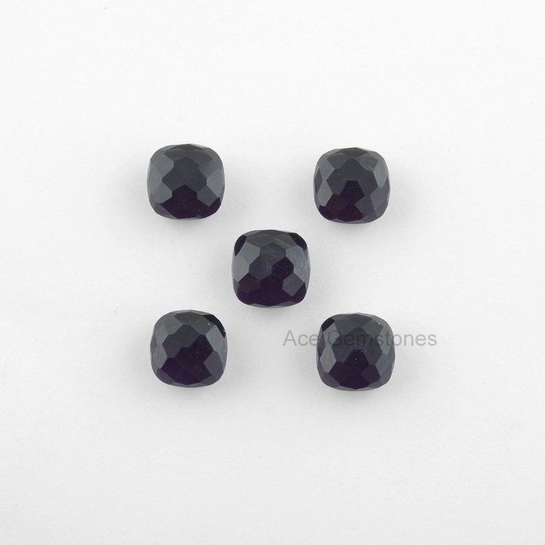 May include: Five black cushion-cut gemstones on a white background.