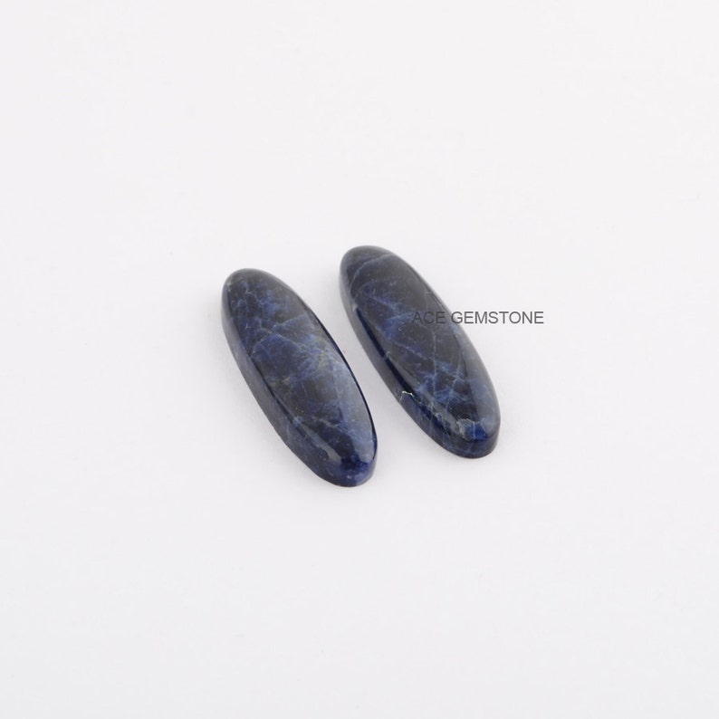 May include: Two oval-shaped, blue sodalite cabochons with a marbled pattern.  ACE GEMSTONE is printed in white text on the background.