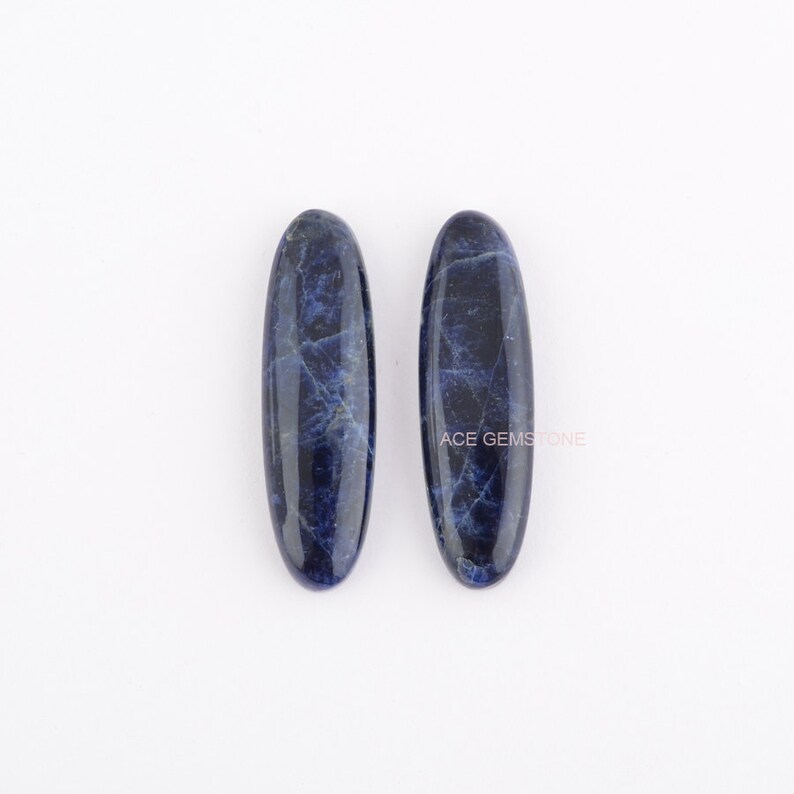 May include: Two oval-shaped, dark blue, polished, natural sodalite stones. The stones have a marbled pattern.