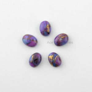 May include: Five oval-shaped purple and gold gemstone cabochons. The stones have a marbled pattern with gold flecks.