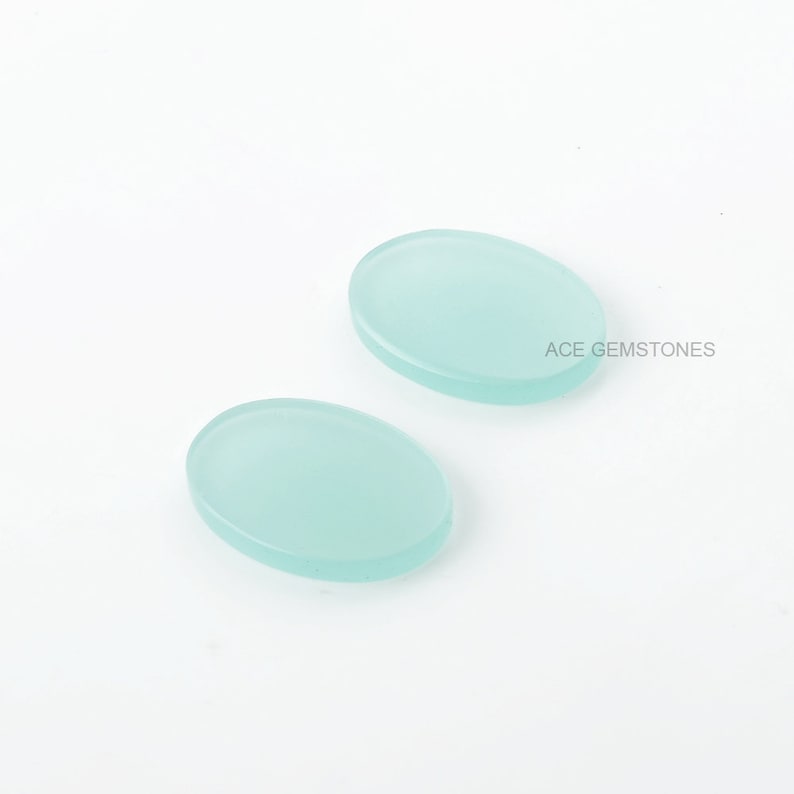 May include: Two oval-shaped, light blue cabochon gemstones. The gemstones are smooth and translucent.