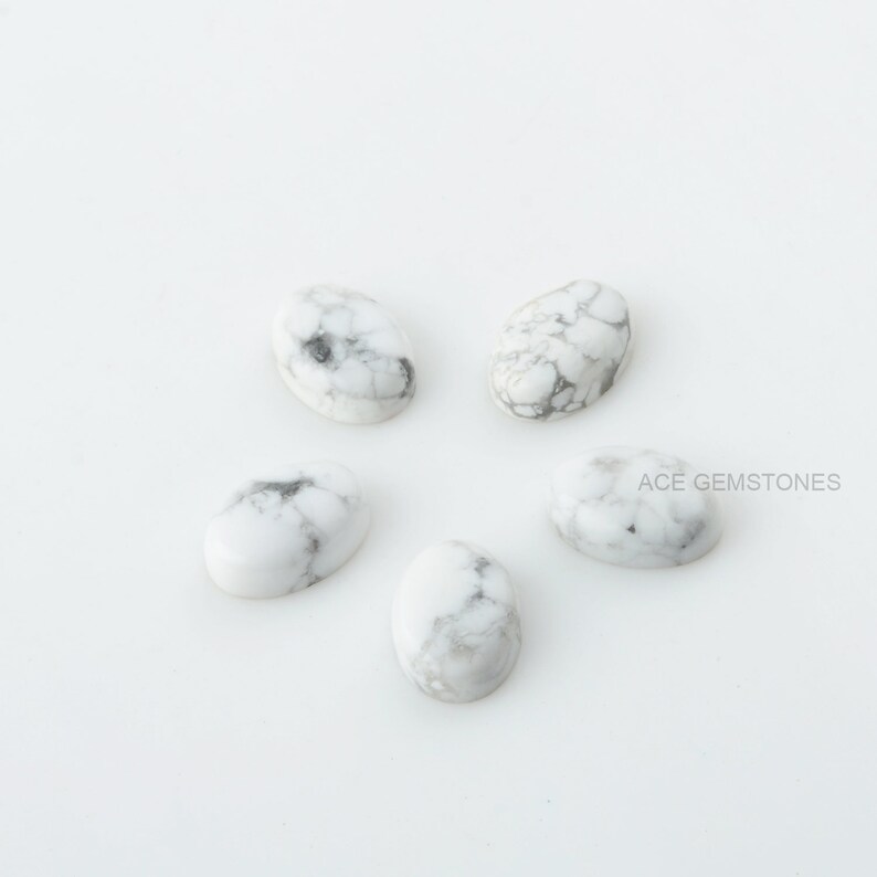 May include: Five white oval cabochon gemstones with gray veining. The stones are arranged in a circular pattern on a white background.