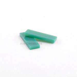 Puede incluir: Dos piedras preciosas rectangulares de cabujón verde, talladas y pulidas, sobre un fondo blanco.