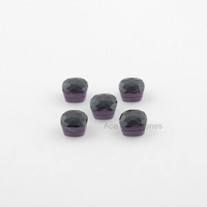 May include: Five dark purple faceted gemstones, each with a square shape, are arranged in a cross pattern on a white background.