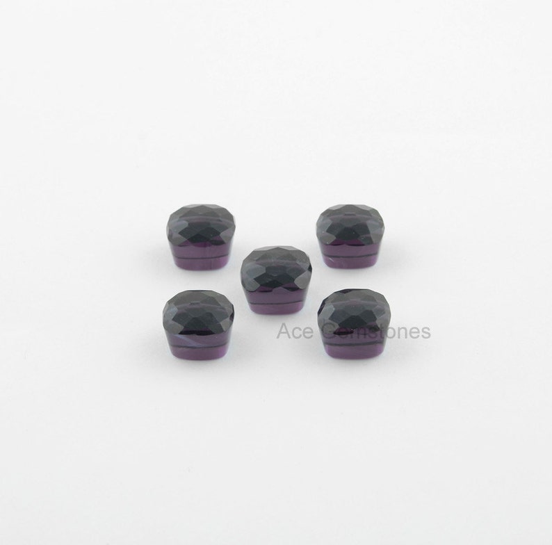 May include: Five dark purple faceted gemstones, each with a square shape, are arranged in a cross pattern on a white background.