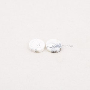 May include: Two round white opal cabochons with black and gray inclusions. The cabochons are approximately 10mm in diameter.