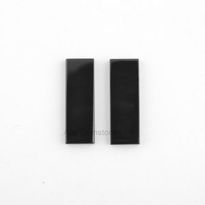 May include: Two black rectangular gemstone cabochons. The cabochons are smooth and polished.