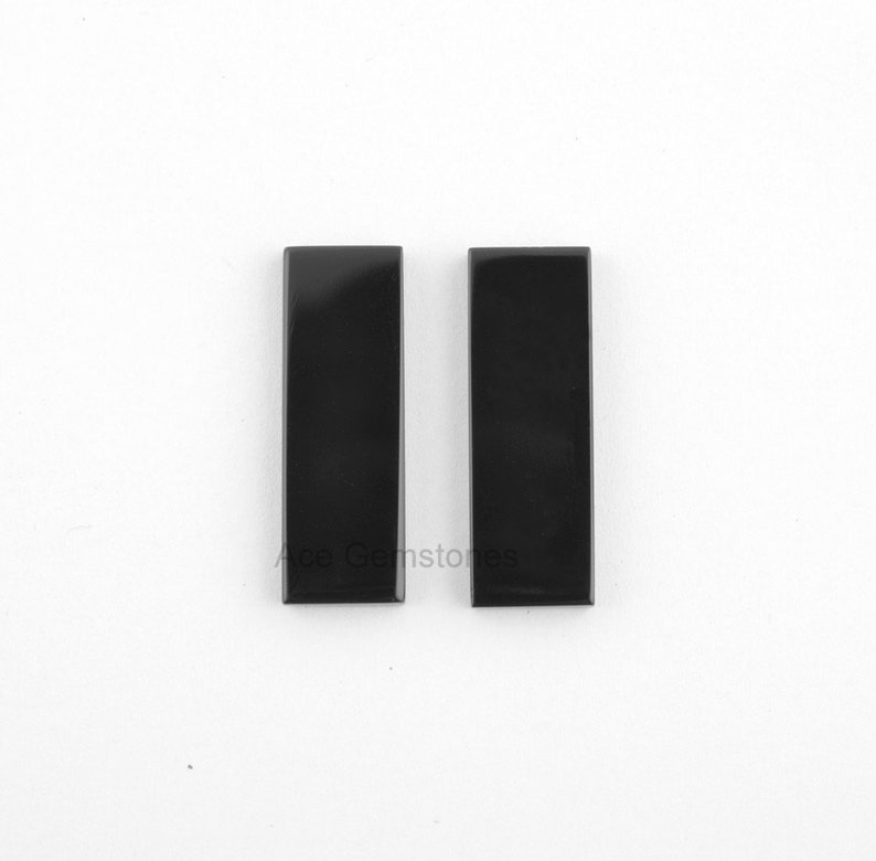 May include: Two black rectangular gemstone cabochons. The cabochons are smooth and polished.