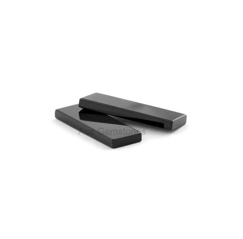 May include: Two black rectangular pieces of polished obsidian, a type of volcanic glass, are stacked on top of each other. The pieces are smooth and shiny.