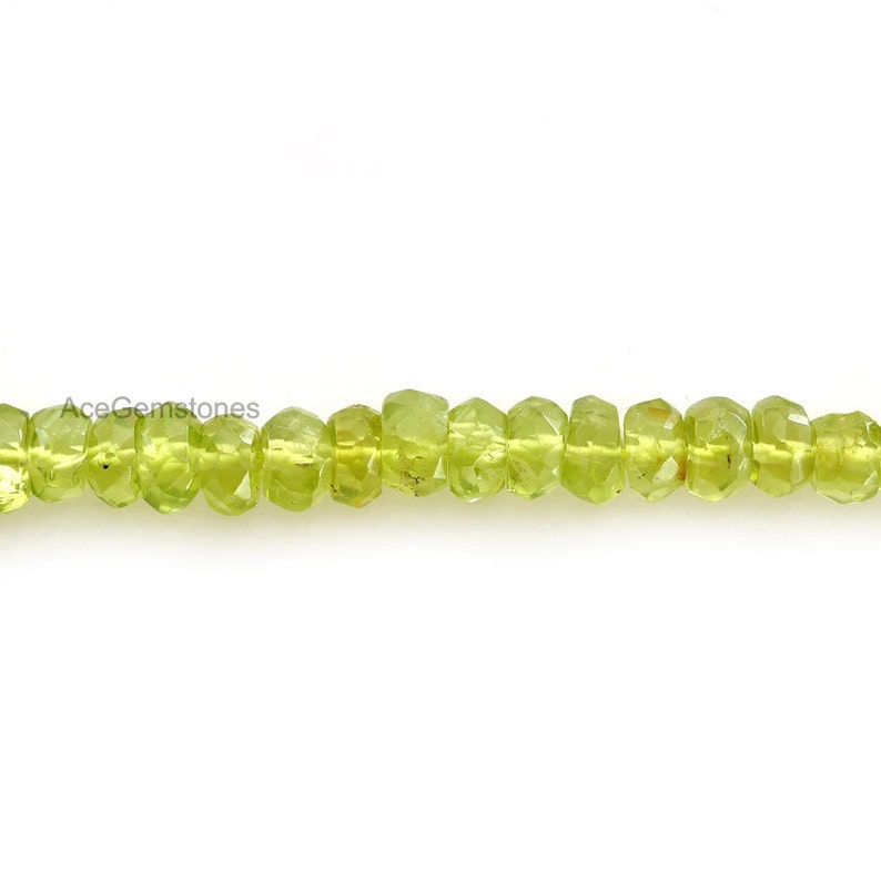 May include: A strand of light green peridot beads, faceted and round, strung together on a white background.
