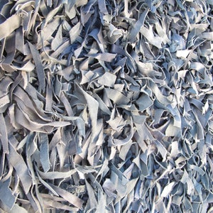May include: A close-up of a pile of light blue leather scraps. The leather is cut into long, thin strips and is arranged in a random pattern.
