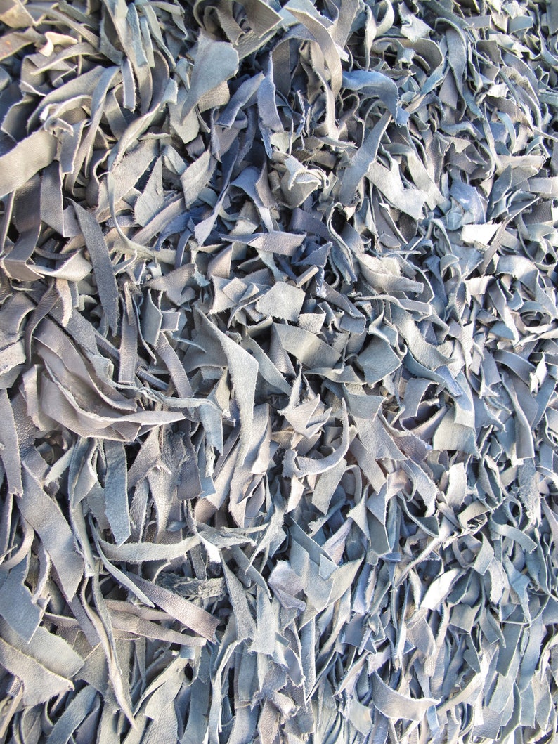May include: A close-up of a pile of light blue leather scraps. The leather is cut into long, thin strips and is arranged in a random pattern.