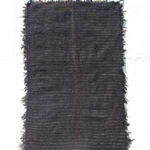 May include: A black woven rug with a fringed edge. The rug has a simple, minimalist design and is made from natural fibers.