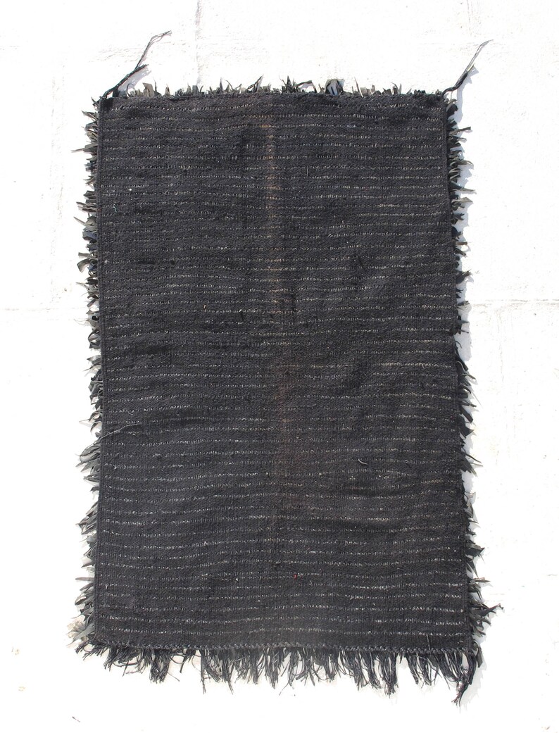 May include: A black woven rug with a fringed edge. The rug has a simple, minimalist design and is made from natural fibers.